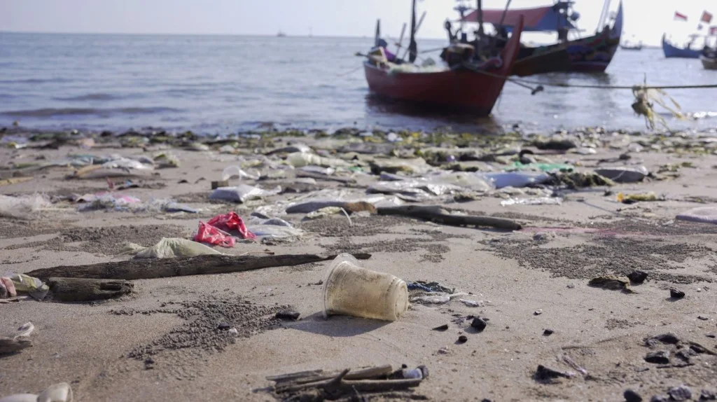 Plastic waste washed up on a beach in Jepara, with fishing boats offshore